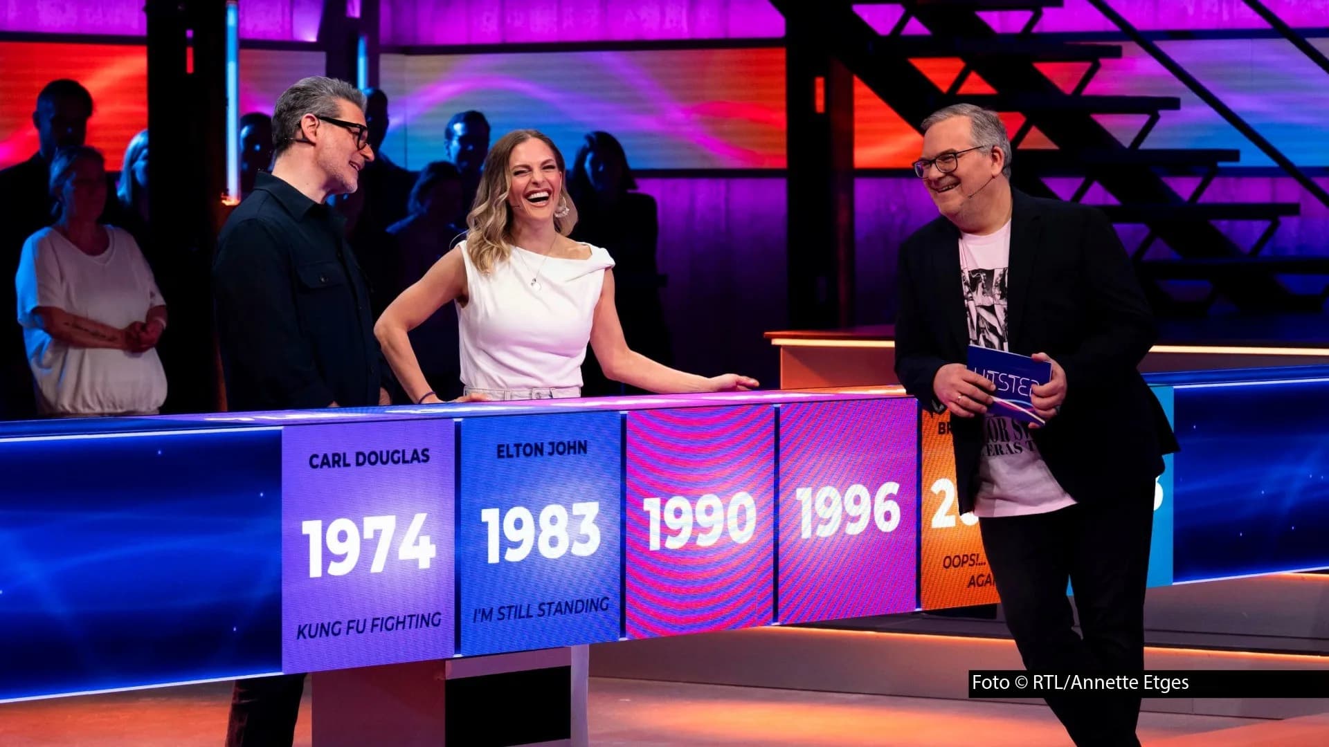 Hans Sigl Bergdoktor: Spielszene aus der RTL-Musikshow Hitster: Zwei Promis und Moderator Elton stehen am leuchtenden