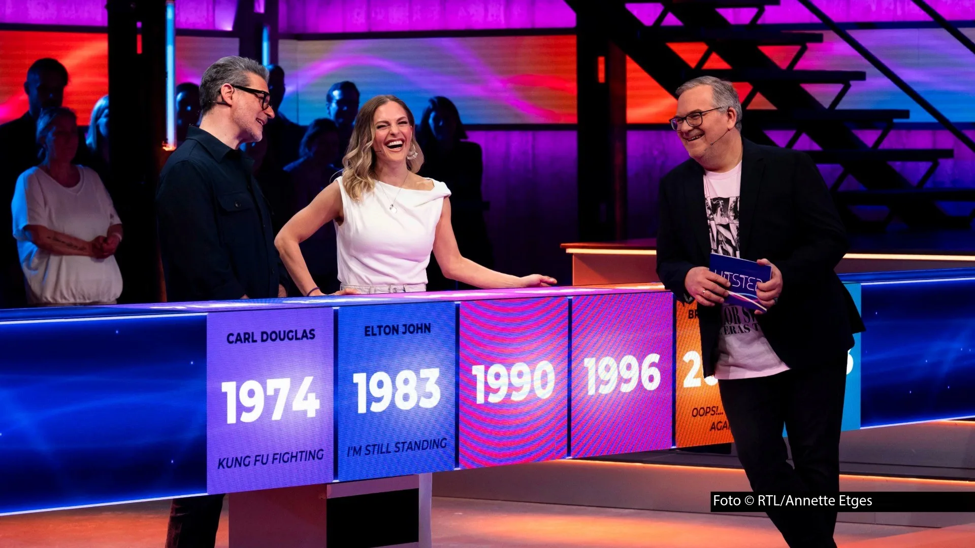 Hans Sigl Bergdoktor: Spielszene aus der RTL-Musikshow Hitster: Zwei Promis und Moderator Elton stehen am leuchtenden